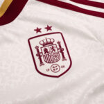 Detalle del escudo bordado con dos estrellas en la camiseta visitante de España 2026. Segunda equipación oficial de la selección.