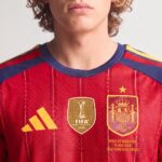 Primer plano de la camiseta de fútbol de España, primera equipación Mundial 2026, con la estrella de campeón sobre el escudo.