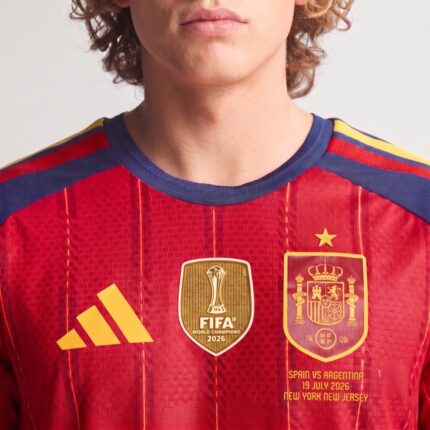 Primer plano de la camiseta de fútbol de España, primera equipación Mundial 2026, con la estrella de campeón sobre el escudo.