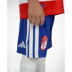 Primera equipación del Granada CF para niños temporada 2026-27. Conjunto de camiseta y pantalón oficial para los más pequeños.